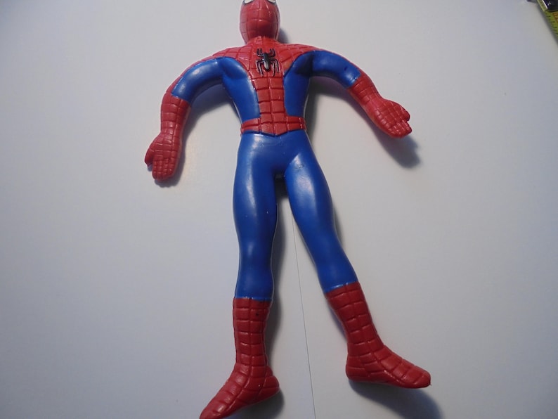 May include: A flexible action figure of a superhero character with a red and blue suit. The figure features a black spider emblem on the chest, a web-like pattern on the red sections of the head, shoulders, and lower legs, and a smooth blue torso.
