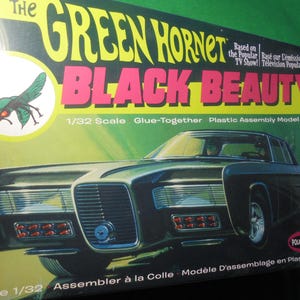 May include: A model kit box for the Black Beauty car from The Green Hornet TV show. The box features the car in a dark color, with the words "The Green Hornet" in yellow and "Black Beauty" in pink. The box also includes an image of a green hornet.