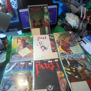 May include: A collection of comic books featuring the title "Faust". The covers display various illustrations with bold colors, including images of demons, figures, and graphic art. Some comics are sealed in plastic.