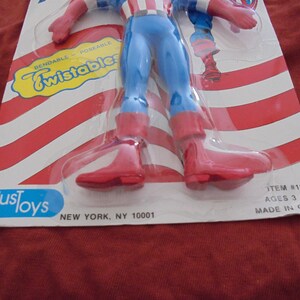May include: A Captain America action figure in a plastic package. The figure is wearing a blue and red costume with red boots and gloves. The packaging has red and white stripes and the words "Bendable Poseable Twistables".