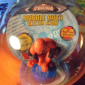 May include: A clear plastic bubble bath glitter globe featuring a red and black Spider-Man figure. The packaging includes text that reads "Bubble Bath Glitter Globe" and "Fill me with water & glitter."
