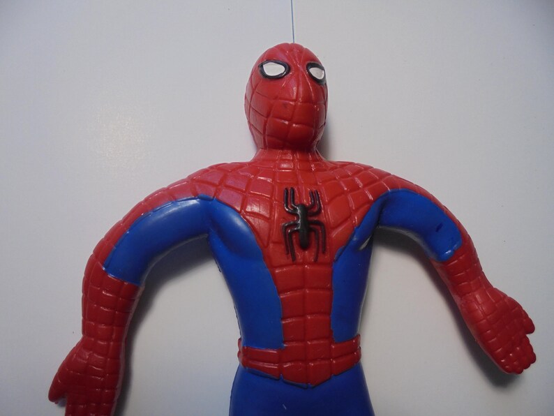 May include: A red and blue Spider-Man action figure featuring a black spider emblem on the chest. The figure has a textured web pattern across the red sections of the head, shoulders, and torso, with white eye lenses and a smooth blue midsection.