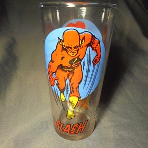 May include: A clear glass featuring a running superhero, The Flash, in orange and yellow against a blue background. The word "FLASH" is printed in red at the bottom of the glass. A vintage comic book collectible.