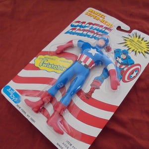 May include: A Captain America action figure in its original packaging. The figure is blue, red, and white, with the words "Captain America" and "Twistable" on the packaging. The packaging also includes the text "50th Anniversary Collectors Edition."