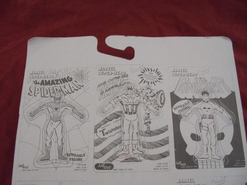 May include: A white cardboard backing featuring three Marvel Super-Hero action figure designs. The figures are The Amazing Spider-Man, Captain America, and The Punisher. Each figure is outlined in black and labeled with the character's name.