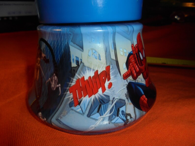 May include: A blue and white tumbler featuring Spider-Man in action. The design includes comic book style graphics of buildings and the word "THWIP!" in red. The tumbler has a blue lid.