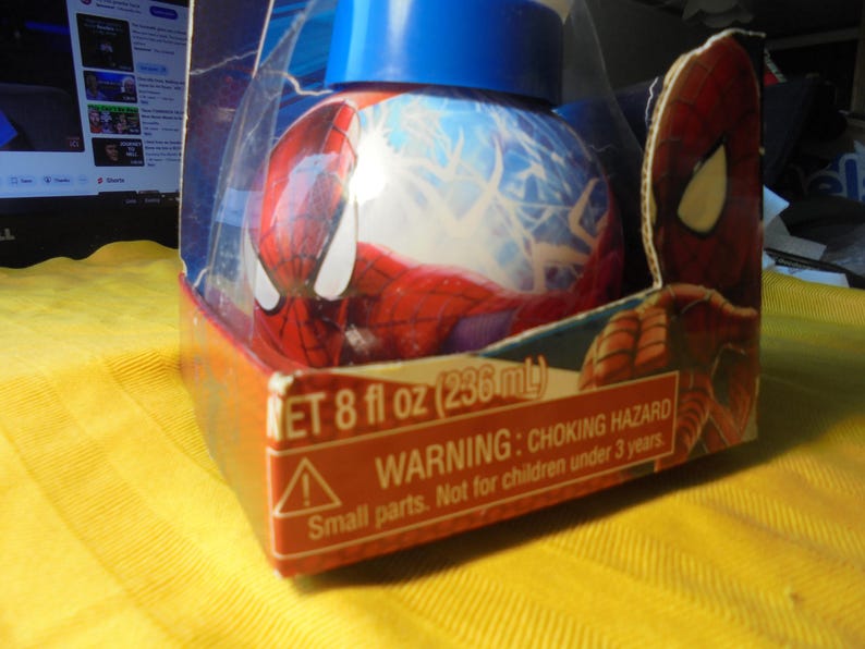 May include: A round Spider-Man themed container with a blue lid, encased in a cardboard box featuring Spider-Man graphics. The packaging displays the text NET 8 fl oz (236 mL) and a warning about a choking hazard for children under 3 years.