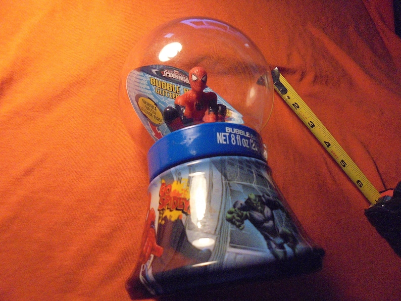 May include: A Spider-Man bubble gum container with a clear plastic globe top. The base is blue and features comic book art of Spider-Man and the Hulk. The container is approximately 6 inches tall and holds 8 fl oz of bubble gum.
