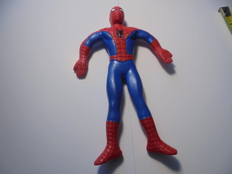 May include: A red and blue Spider-Man action figure with a black spider emblem on the chest. The figure features a web pattern on the red sections of the head, shoulders, and boots. A yellow measuring tape is visible in the upper right corner.