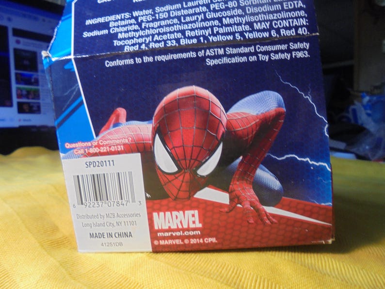 May include: A blue cardboard product box featuring a graphic of the Marvel character Spider-Man in a crouching pose. The box includes a barcode, the text Marvel, and a list of ingredients printed in white against a dark blue background.