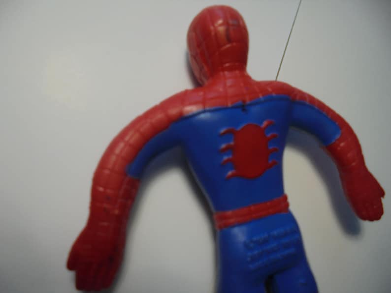 May include: A red and blue plastic Spider-Man action figure shown from the back. The figure features a red head and arms with a black web pattern, a blue torso with a red spider emblem on the back, and blue legs with a red belt detail.