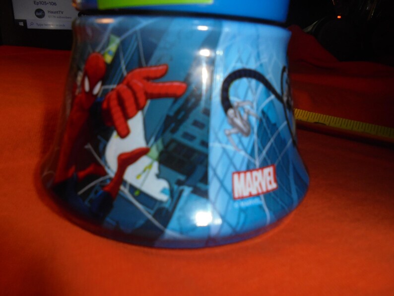 May include: A blue Marvel-branded tumbler featuring Spider-Man. The design includes Spider-Man in action with red and white accents against a cityscape backdrop. The tumbler has a blue lid and a curved shape.