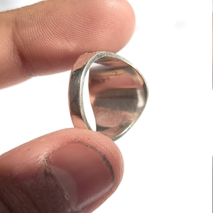 May include: A silver ring with a rounded, slightly curved top. The ring is shown on a finger.