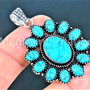 May include: A silver pendant featuring a large central oval turquoise stone surrounded by twelve smaller oval turquoise stones. The stones are bright blue with dark veining, set in a decorative silver frame with a twisted rope border.