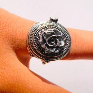 K&ouml;nnte beinhalten: Ein silberner Ring mit einem ovalen, klappbaren Anh&auml;nger mit einem detaillierten Rosenmotiv.