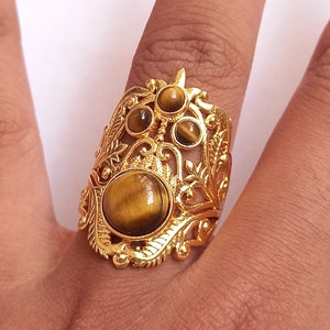 May include: Gold ring with a large tiger's eye stone surrounded by smaller stones and intricate floral designs.