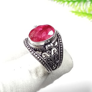May include: A silver ring featuring an oval-cut, deep red gemstone. The ring has an ornate, detailed design with a textured band and decorative filigree. The gemstone is the focal point, set in a raised bezel.