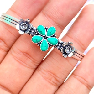 May include: Silver bangle bracelet with three flower accents. The center flower has a turquoise stone.