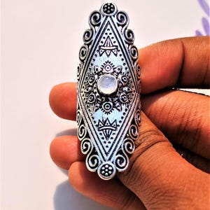 May include: A silver ring with a white moonstone set in a geometric design. The ring is ornate and has a detailed pattern.