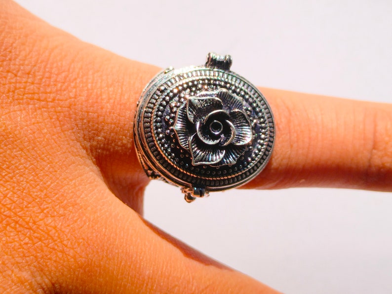 K&ouml;nnte beinhalten: Ein silberner Ring mit einem ovalen, klappbaren Anh&auml;nger mit einem detaillierten Rosenmotiv.