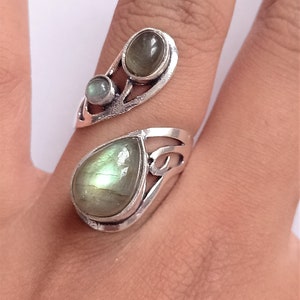 Könnte beinhalten: Ein silberner Ring mit einem tropfenförmigen grünen Edelstein und zwei kleineren runden grünen Edelsteinen. Der Ring ist so konzipiert, dass er sich um den Finger wickelt.