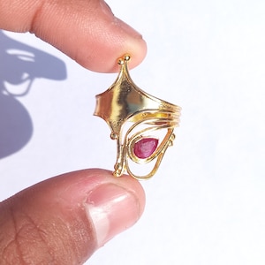 Op de afbeelding: Een gouden ring met een rode edelsteen in het midden. De ring heeft een uniek, ingewikkeld ontwerp met meerdere lagen metaal.