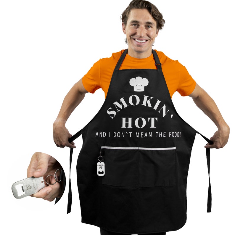 Puede incluir: Delantal negro con texto blanco que dice "Smokin' Hot and I don't mean the food!" Un gr&aacute;fico de gorro de chef blanco est&aacute; por encima del texto. El delantal tiene un bolsillo con un abridor de botellas adjunto.