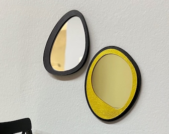 Peut inclure: Deux miroirs décoratifs, l'un noir et l'autre doré, accrochés à un mur blanc. Les miroirs sont en forme d'ovales et ont un design moderne.