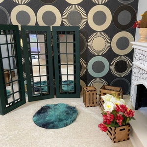 May include: A set of three green framed mirrors with a grid pattern, a teal rug, and a white fireplace with a stone facade. There are also two wooden crates and a bouquet of red and white flowers in a wooden planter.