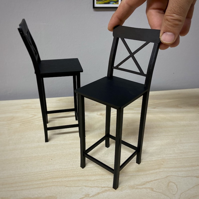 May include: Two black metal bar stools with a simple, modern design. The stools have a square base and a cross-shaped back.