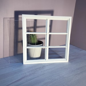 Könnte beinhalten: Weißer Miniatur-Fensterrahmen mit sechs Fensterscheiben, in dem sich eine kleine Topfpflanze mit Kaktus befindet. Der Fensterrahmen steht auf einer hellen Holzoberfläche.