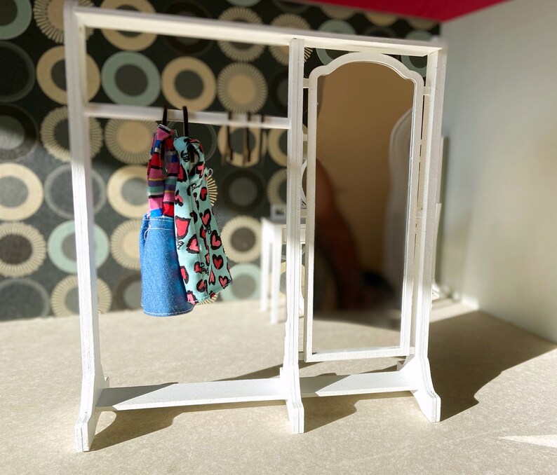 Peut inclure: Un portant &agrave; v&ecirc;tements en bois blanc avec un miroir et deux robes suspendues. Une robe est bleue &agrave; pois blancs et l'autre est rose &agrave; c&oelig;urs blancs.
