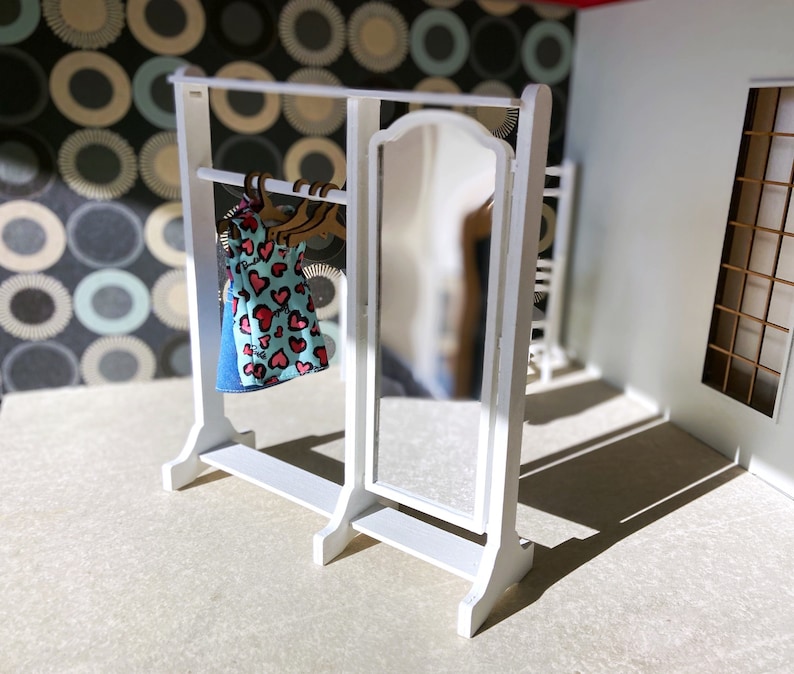 Peut inclure: Un portant &agrave; v&ecirc;tements en bois blanc avec un miroir et une &eacute;tag&egrave;re. Une robe bleue et blanche avec des c&oelig;urs rouges est accroch&eacute;e au portant.