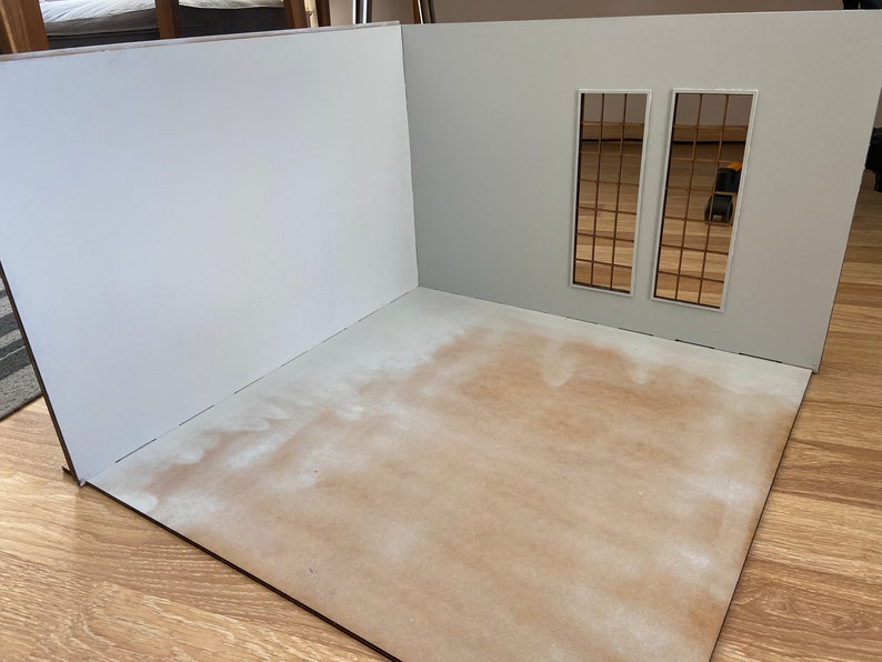 May include: A white room with two windows, each with a grid pattern. The room is empty except for a brown floor.