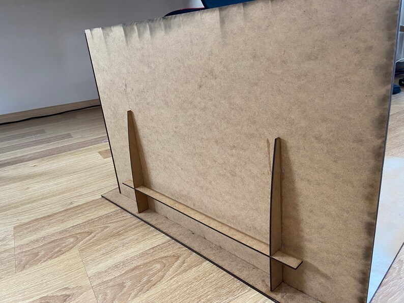 May include: A brown cardboard easel with two vertical supports and a horizontal base. The easel is designed to hold a sign or a piece of art.