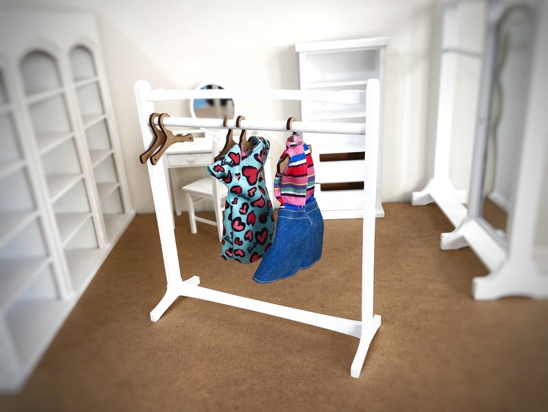 Puede incluir: Un perchero de madera blanco con dos perchas que sostienen un vestido azul y blanco con corazones rosas y una falda vaquera azul con una camisa a rayas.