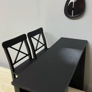 Pu&ograve; includere: Un tavolo nero con due sedie nere. Il tavolo ha un piano rettangolare e un design semplice. Le sedie hanno uno schienale a croce.