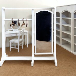 Peut inclure: Un portant &agrave; v&ecirc;tements en bois blanc avec un miroir et une &eacute;tag&egrave;re. Le portant a une barre en m&eacute;tal pour accrocher les v&ecirc;tements et des cintres en bois.