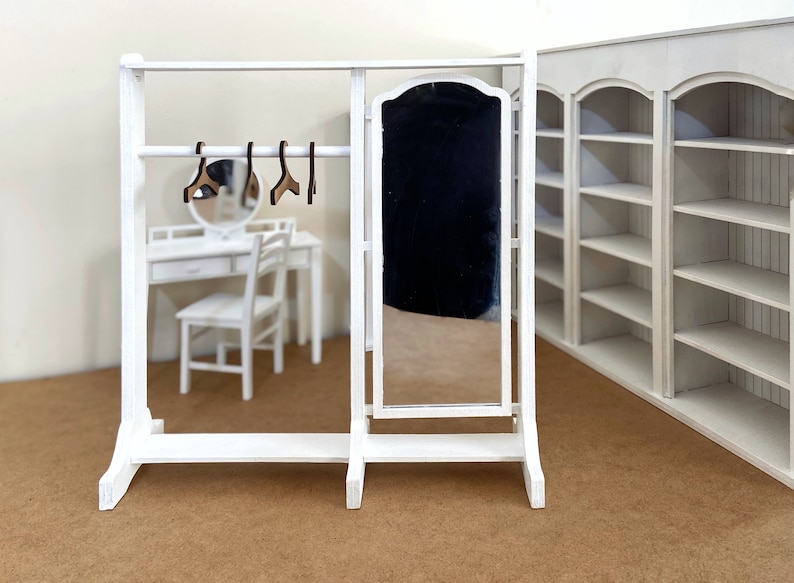 Peut inclure: Un portant &agrave; v&ecirc;tements en bois blanc avec un miroir et une &eacute;tag&egrave;re. Le portant a une barre en m&eacute;tal pour accrocher les v&ecirc;tements et des cintres en bois.