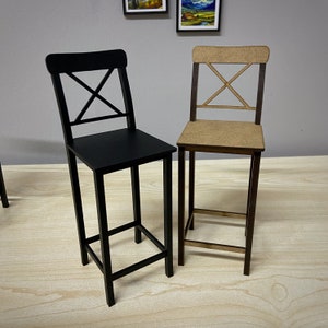 May include: Two wooden chairs with a black and a natural wood finish. Both chairs have a simple, modern design with a cross-shaped back.