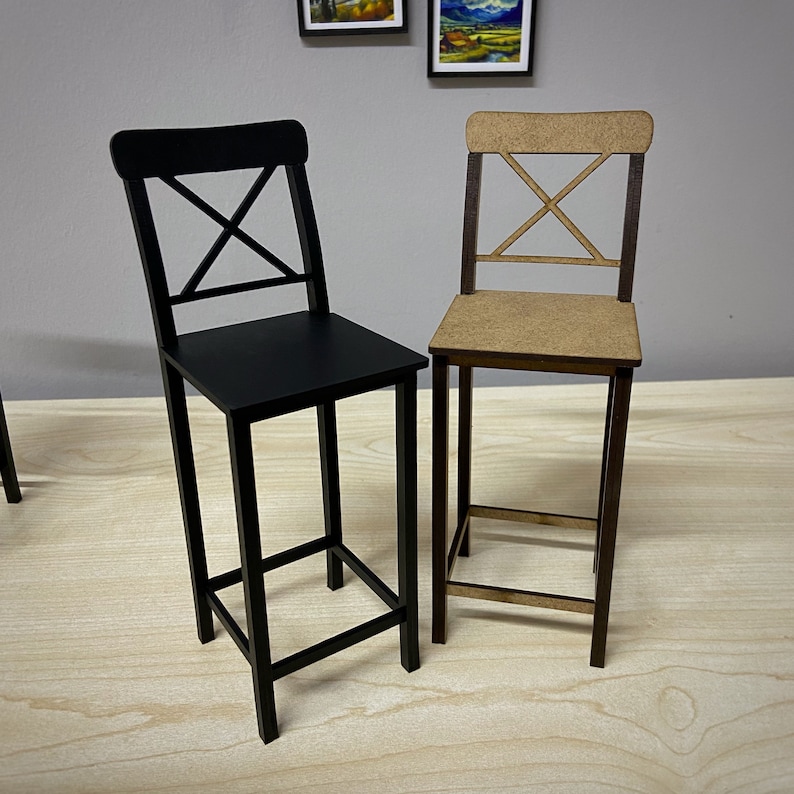 May include: Two wooden chairs with a black and a natural wood finish. Both chairs have a simple, modern design with a cross-shaped back.