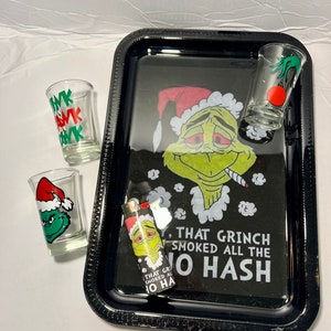 May include: Black rolling tray featuring a green Grinch character wearing a Santa hat and holding a joint. The tray has the text "That Grinch Smoked All The Hash". The tray comes with three shot glasses and a lighter, all featuring the Grinch character.