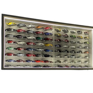 Könnte beinhalten: Eine schwarze Vitrine mit Reihen von Miniatur-Spielzeugautos. Die Autos sind in verschiedenen Farben, darunter Rot, Gelb, Blau und Silber. Das Gehäuse hat einen schwarzen Rahmen und eine eingebaute Beleuchtung.