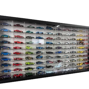 Può includere: Una grande vetrina nera piena di numerose macchinine giocattolo di vari colori e design. Le auto sono disposte su più ripiani, creando una collezione completa. La vetrina ha un fronte trasparente.