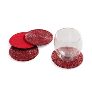 May include: A set of four red beaded coasters, with a wine glass resting on one. The coasters are round and have a textured surface. The coasters are a deep red color.