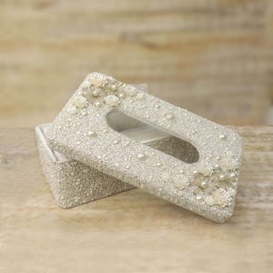 May include: A white tissue box cover with a pearl and floral design. The cover is open and the inside is white.