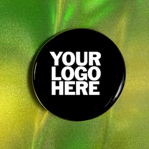 Op de afbeelding: Een ronde zwarte knop met witte tekst die "YOUR LOGO HERE" zegt op een groene en gele achtergrond.