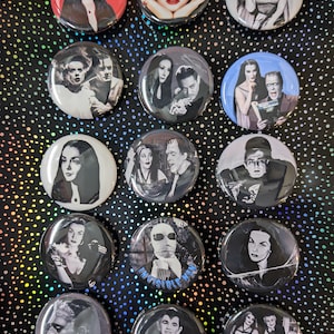 Puede incluir: Un conjunto de 15 botones redondos con imágenes de personajes de películas y programas de televisión de terror clásicos. Los botones presentan imágenes en blanco y negro de personajes como los Munsters, el Hombre Invisible y Drácula.