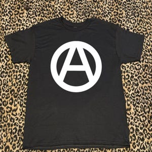 Peut inclure: T-shirt noir avec un symbole d'anarchie blanc imprimé sur le devant.