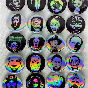 May include: A set of 16 horror movie character buttons with iridescent holographic backgrounds. The buttons feature characters from films such as "The Exorcist", "Friday the 13th", "28 Weeks Later", "The Texas Chainsaw Massacre", "Halloween", "IT", "Scream", and "Chucky".